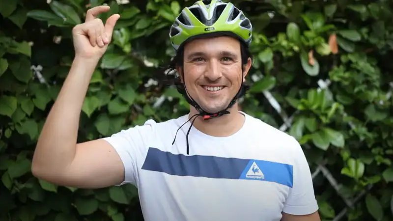 Ein American Express Mitarbeiter mit grünem Fahrradhelm vor einer grünen Hecke