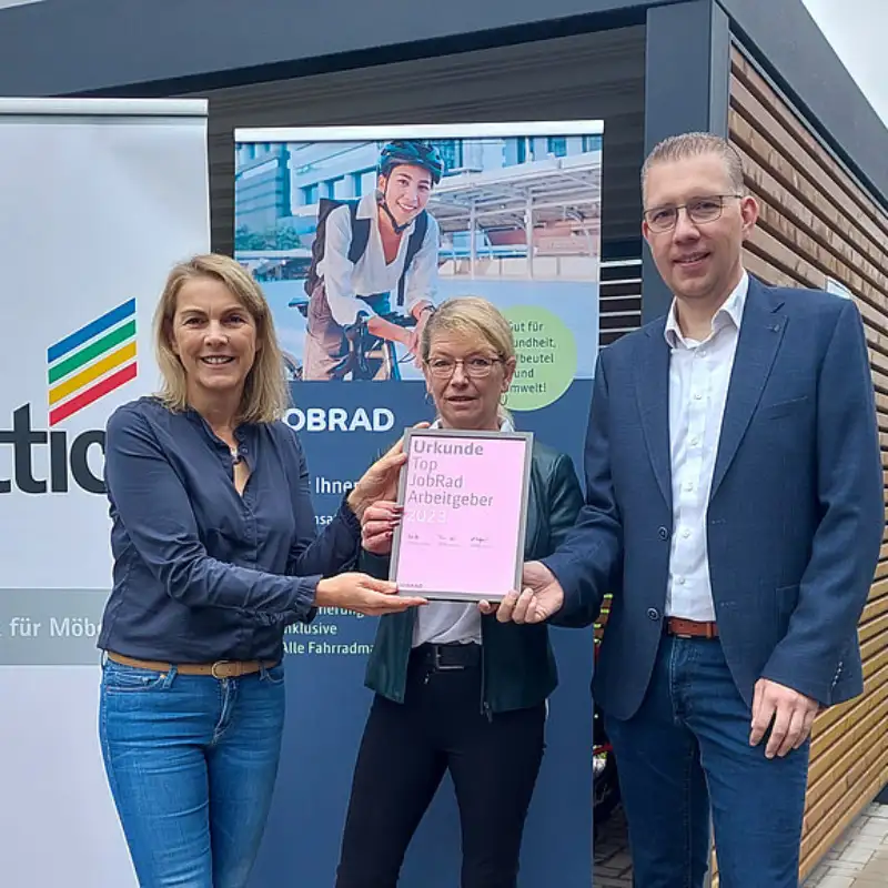 Monika Titze, von der Hettich Gruppe, steht zusammen mit einer Frau und einem Mann vor einem Poster mit dem Schriftzug Hettich und dem Hettich Logo. Sie alle tragen blaue Geschäftskleidung Monika Titze, von der Hettich Gruppe, steht zusammen mit einer Frau und einem Mann vor einem Poster mit dem Schriftzug Hettich und dem Hettich Logo. Sie alle tragen blaue Geschäftskleidung